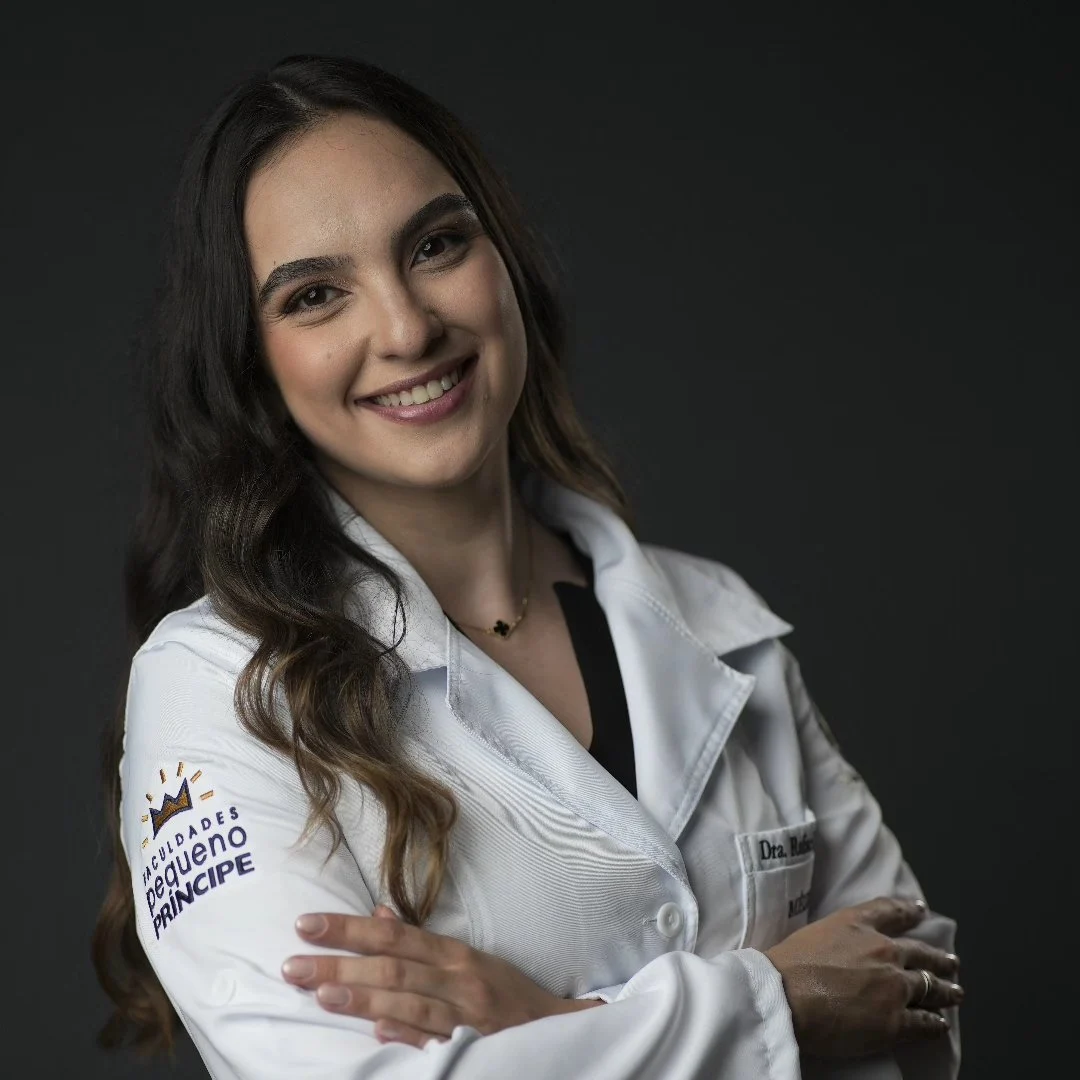 Dra. Rafaela Julião, médica, de jaleco branco, sorrindo com os braços cruzados.